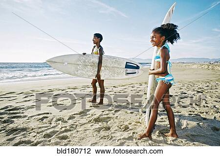 Stock Image - Black mother and daughter carrying surfboards on beach. Fotosearch