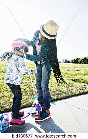 Stock Photo - Black mother fastening helmet on daughter. Fotosearch