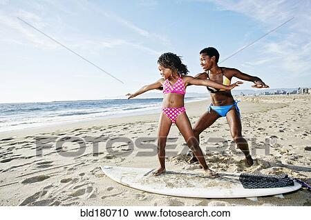 Black mother teaching daughter to surf on beach View Large Photo Image Stock Image - Black mother teaching daughter to surf on beach. Fotosearch