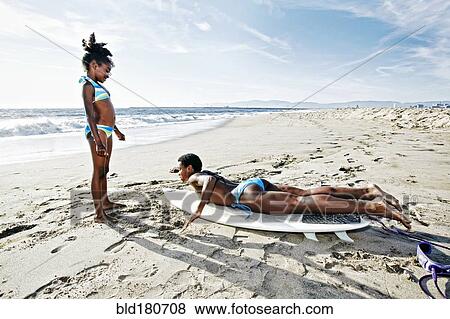 Black mother teaching daughter to surf on beach View Large Photo Image Stock Photo - Black mother teaching daughter to surf on beach. Fotosearch