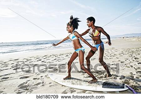 Stock Photo - Black mother teaching daughter to surf on beach. Fotosearch