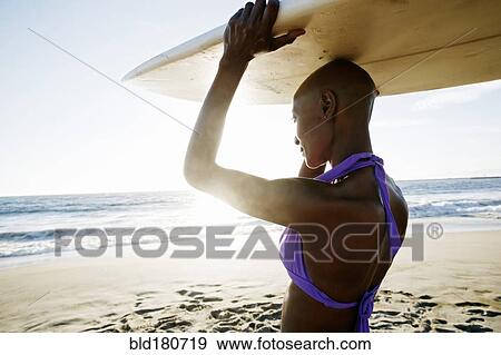 Stock Photo - Black woman carrying surfboard on beach. Fotosearch