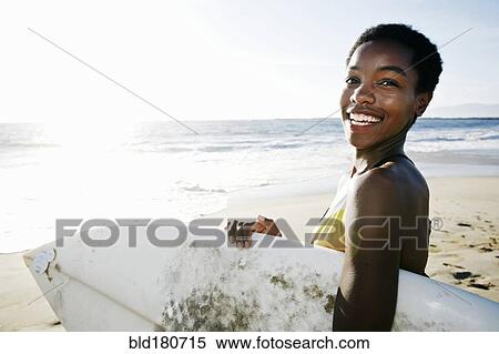 Stock Photography - Black woman carrying surfboard on beach. Fotosearch