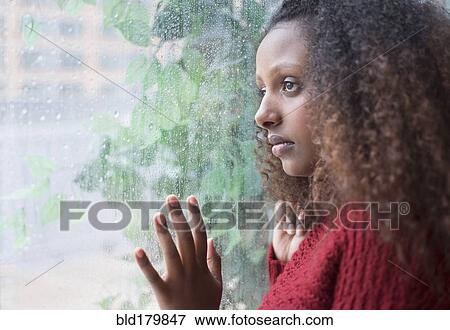Stock Photo - Black woman looking out rainy window. Fotosearch