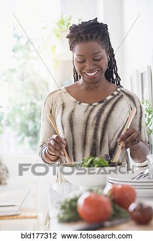 Stock Image - Black woman tossing salad in kitchen. Fotosearch