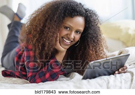 Stock Image - Black woman using digital tablet on bed. Fotosearch