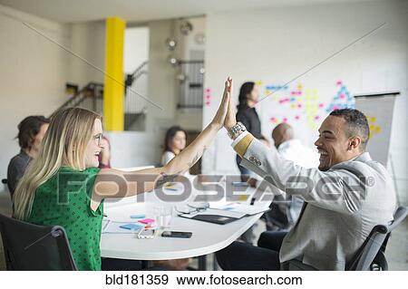 Stock Photo - Business people high-fiving in office meeting. Fotosearch