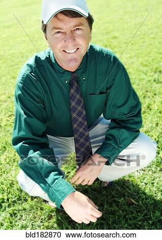 Stock Image - Businessman crouching on grass lawn. Fotosearch