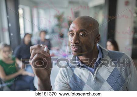 Stock Image - Businessman drawing graph on glass wall in office. Fotosearch