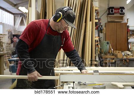 Stock Image - Carpenter using table saw in workshop. Fotosearch
