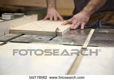 Stock Image - Carpenter using table saw in workshop. Fotosearch