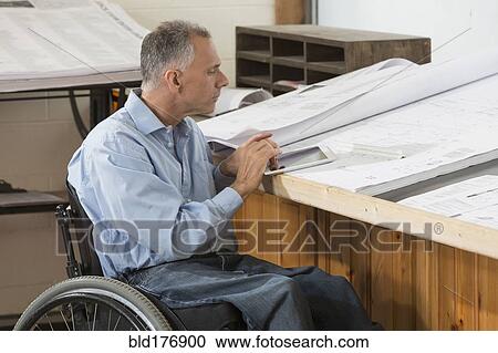 Stock Image - Caucasian architect in wheelchair working in office. Fotosearch