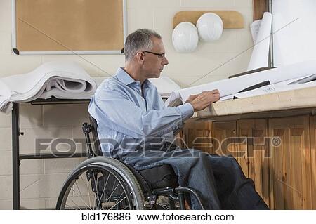 Stock Photograph - Caucasian architect in wheelchair working in office. Fotosearch