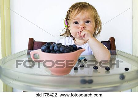 Stock Image - Caucasian baby girl eating blueberries. Fotosearch