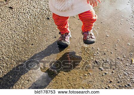 Stock Image - Caucasian baby girl walking in puddle. Fotosearch