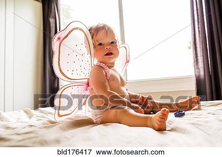 Stock Photo - Caucasian baby girl wearing fairy wings on bed. Fotosearch