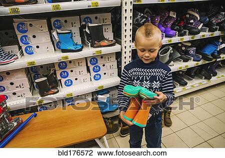 Stock Image - Caucasian boy admiring boots in store. Fotosearch