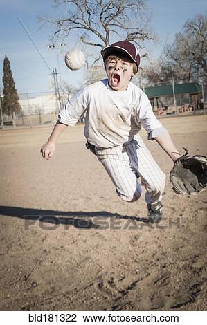 Stock Image - Caucasian boy catching baseball on field. Fotosearch
