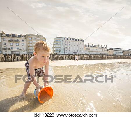 Stock Image - Caucasian boy catching water in pail on beach. Fotosearch