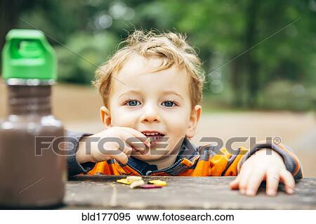 Stock Photography - Caucasian boy eating snack at picnic table. Fotosearch