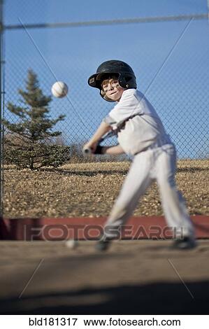 Stock Photo - Caucasian boy hitting baseball on field. Fotosearch