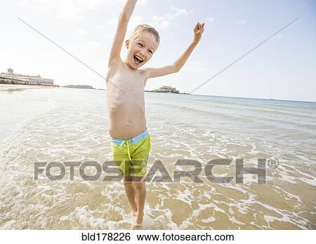 Stock Photograph - Caucasian boy playing in waves on beach. Fotosearch