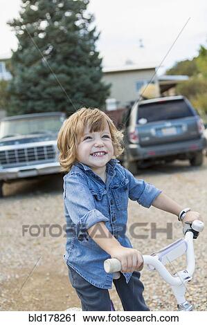 Stock Image - Caucasian boy riding tricycle in gravel. Fotosearch