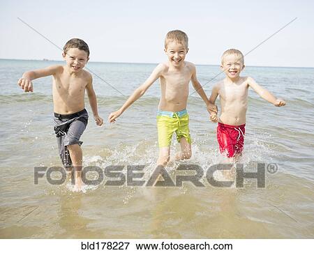 Stock Photo - Caucasian boys playing in waves on beach. Fotosearch