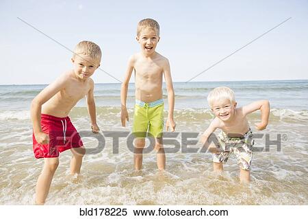 Stock Photography - Caucasian boys playing in waves on beach. Fotosearch