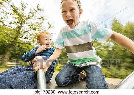 Stock Image - Caucasian boys playing on merry-go-round. Fotosearch