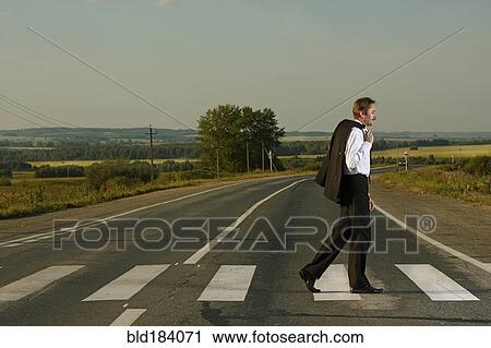 Stock Image - Caucasian businessman crossing rural street. Fotosearch