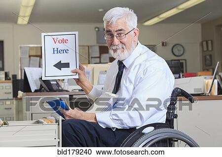 Stock Image - Caucasian businessman holding voting sign in office. Fotosearch