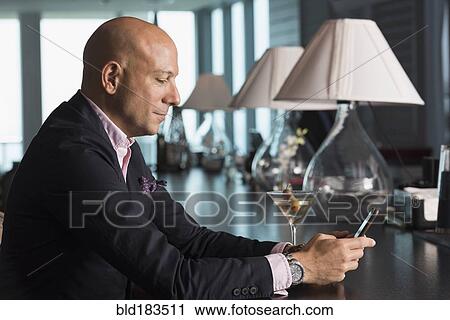 Stock Image - Caucasian businessman using cell phone in bar. Fotosearch