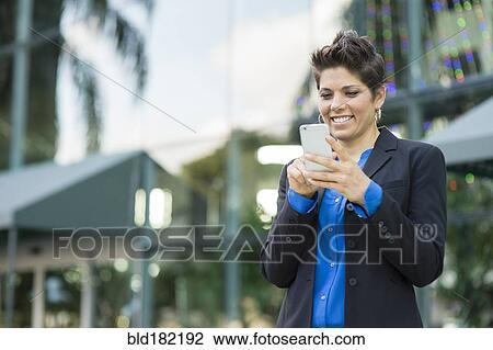 Stock Image - Caucasian businesswoman using cell phone outdoors. Fotosearch