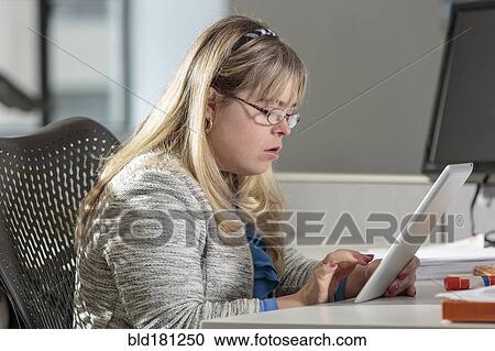 Stock Image - Caucasian businesswoman with Down Syndrome using digital tablet in office. Fotosearch