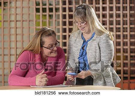 Stock Photograph - Caucasian businesswomen using cell phone in office. Fotosearch
