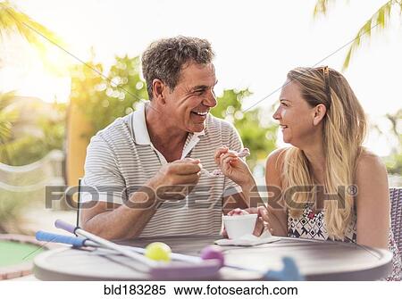 Stock Photography - Caucasian couple eating ice cream at outdoor table. Fotosearch
