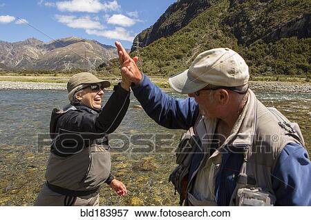 Stock Photo - Caucasian couple high-fiving in remote river. Fotosearch