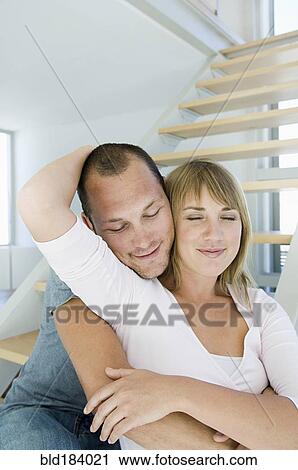 Stock Image - Caucasian couple hugging in modern home. Fotosearch