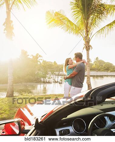 Stock Image - Caucasian couple hugging near convertible. Fotosearch