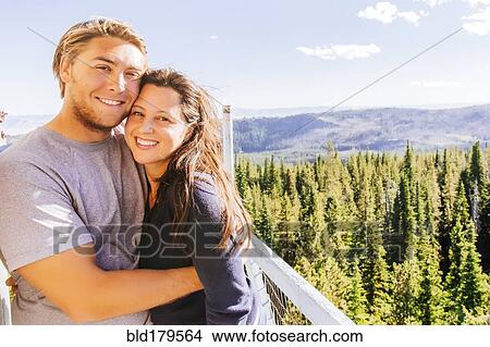 Picture - Caucasian couple hugging over forest treetops. Fotosearch