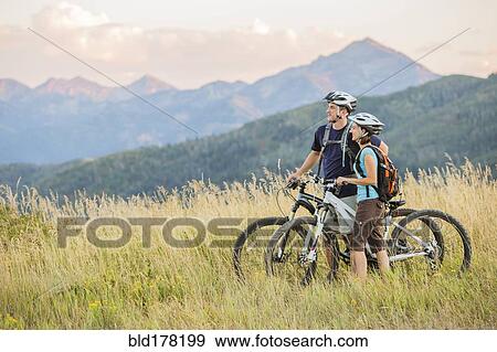 Caucasian couple riding mountain bikes in field View Large Photo Image Stock Photo - Caucasian couple riding mountain bikes in field. Fotosearch
