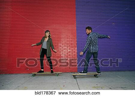 Stock Photo - Caucasian couple riding skateboards on sidewalk. Fotosearch