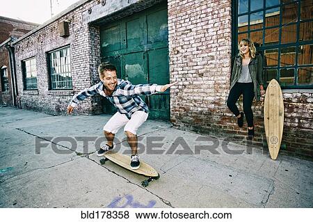 Stock Photo - Caucasian couple skateboarding on sidewalk. Fotosearch