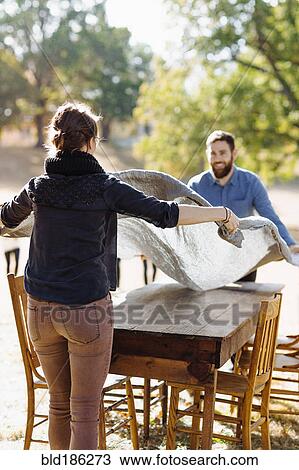 Stock Image - Caucasian couple spreading tablecloth on outdoor table. Fotosearch