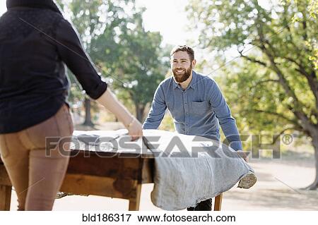 Stock Photo - Caucasian couple spreading tablecloth on outdoor table. Fotosearch