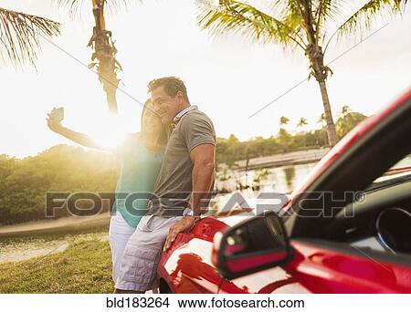 Picture - Caucasian couple taking selfie on convertible. Fotosearch
