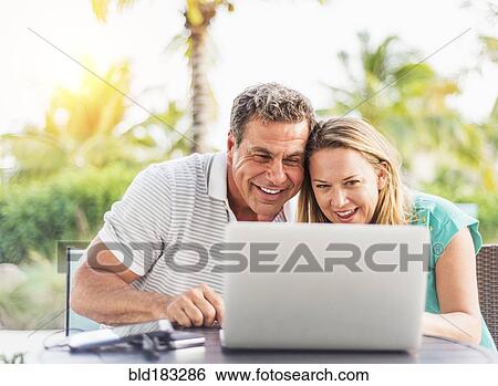 Stock Photograph - Caucasian couple using laptop outdoors. Fotosearch