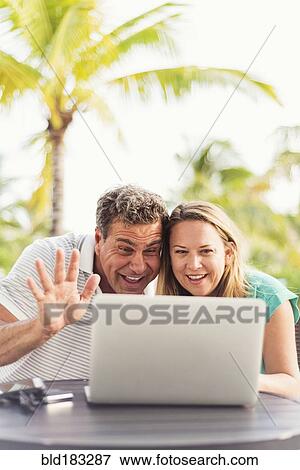 Stock Photo - Caucasian couple video chatting on laptop outdoors. Fotosearch