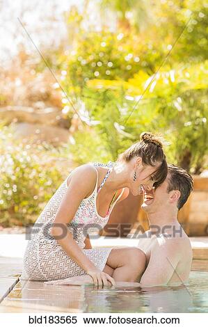 Stock Photography - Caucasian couple whispering in swimming pool. Fotosearch